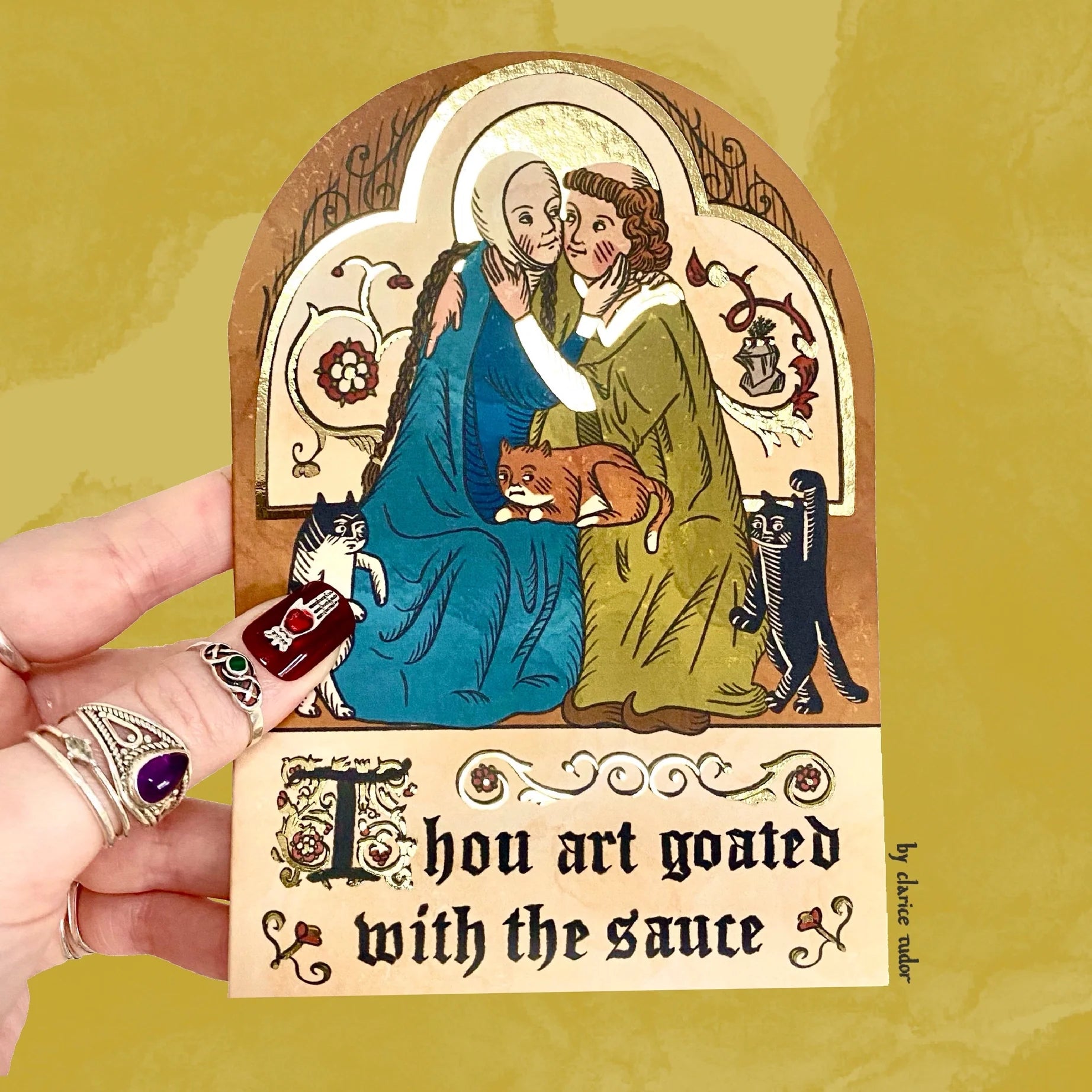 Hand with painted nails and rings holds medieval cat art illustration, text reads Thou art goated with the sauce below.