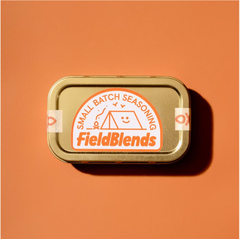 FieldBlends Small Batch Seasoning gold tin with tent and smiling sun illustration, on an orange background. Premium spice blend packaging.