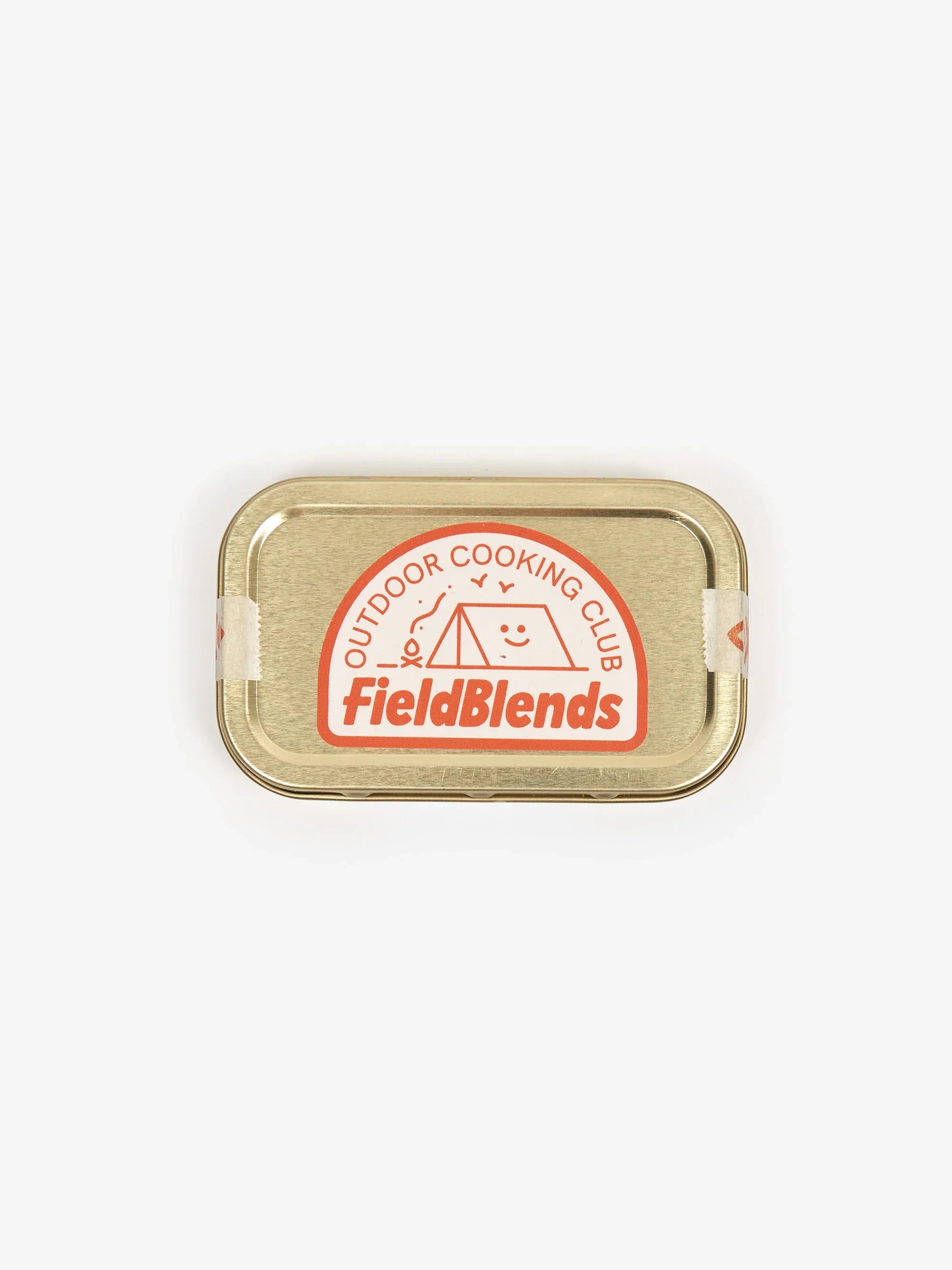 Gold-lidded FieldBlends Outdoor Cooking Club tin with red, white label, tent, and smiley face for camp kitchen gear.