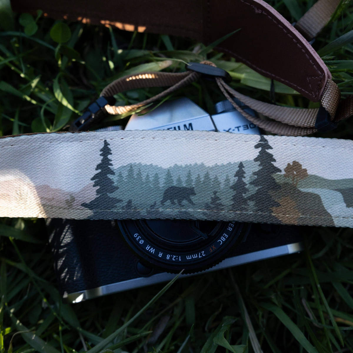 Forager Provisions LTD Wildtree camera strap with wilderness landscape print and brown faux suede backing on grass.