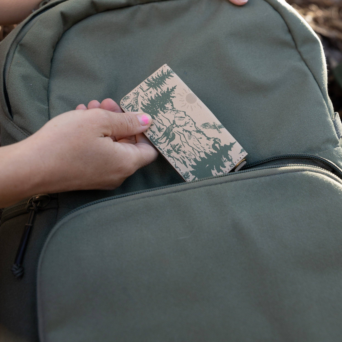 Forager Provisions LTD Wildtree Woodland Landscape card holder being placed into a green backpack pocket.