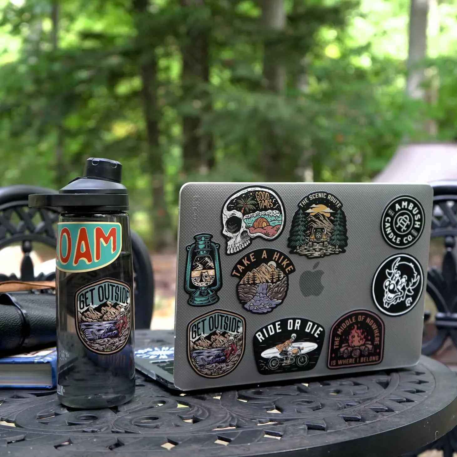 The Ambush Candle Co Get Outside Sticker, featuring the "GET OUTSIDE" text and a mountain scene, is placed among fallen autumn leaves. This weatherproof sticker, made in the USA, can be removed without damage.