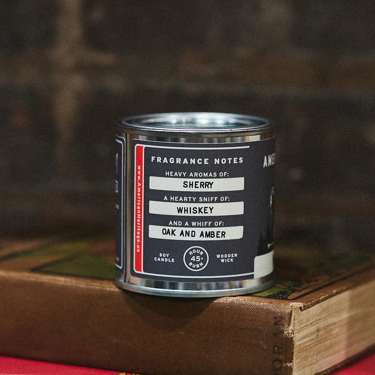 American Heritage Brands Peppered Suede Wood Wick Candle on books, labeled scent notes, cozy dimmed background for ambiance.