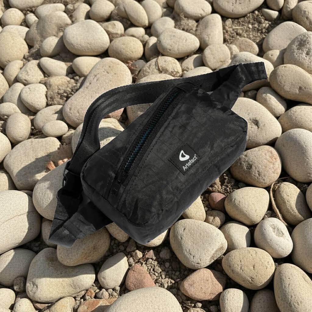 Forager Provisions LTD Artefact Eco black upcycled wind sail banana sling bag on a rocky beach surface