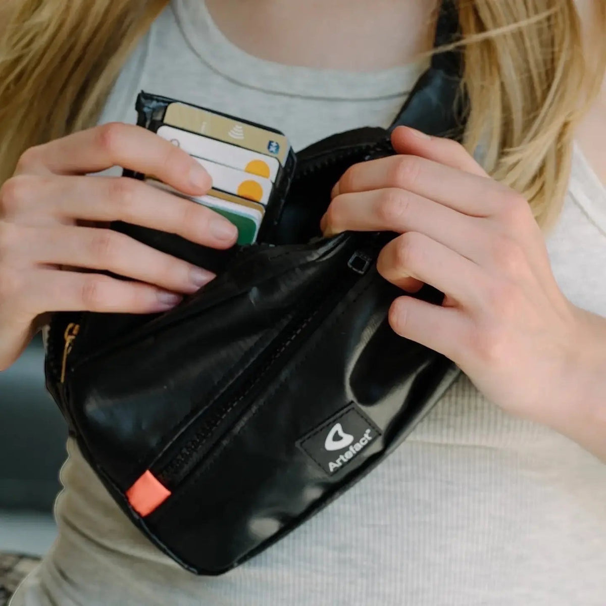 Person inserting cards into a black Artefact Eco Hornbill Banana Sling Bag featuring Artefact logo, stylish eco accessory.