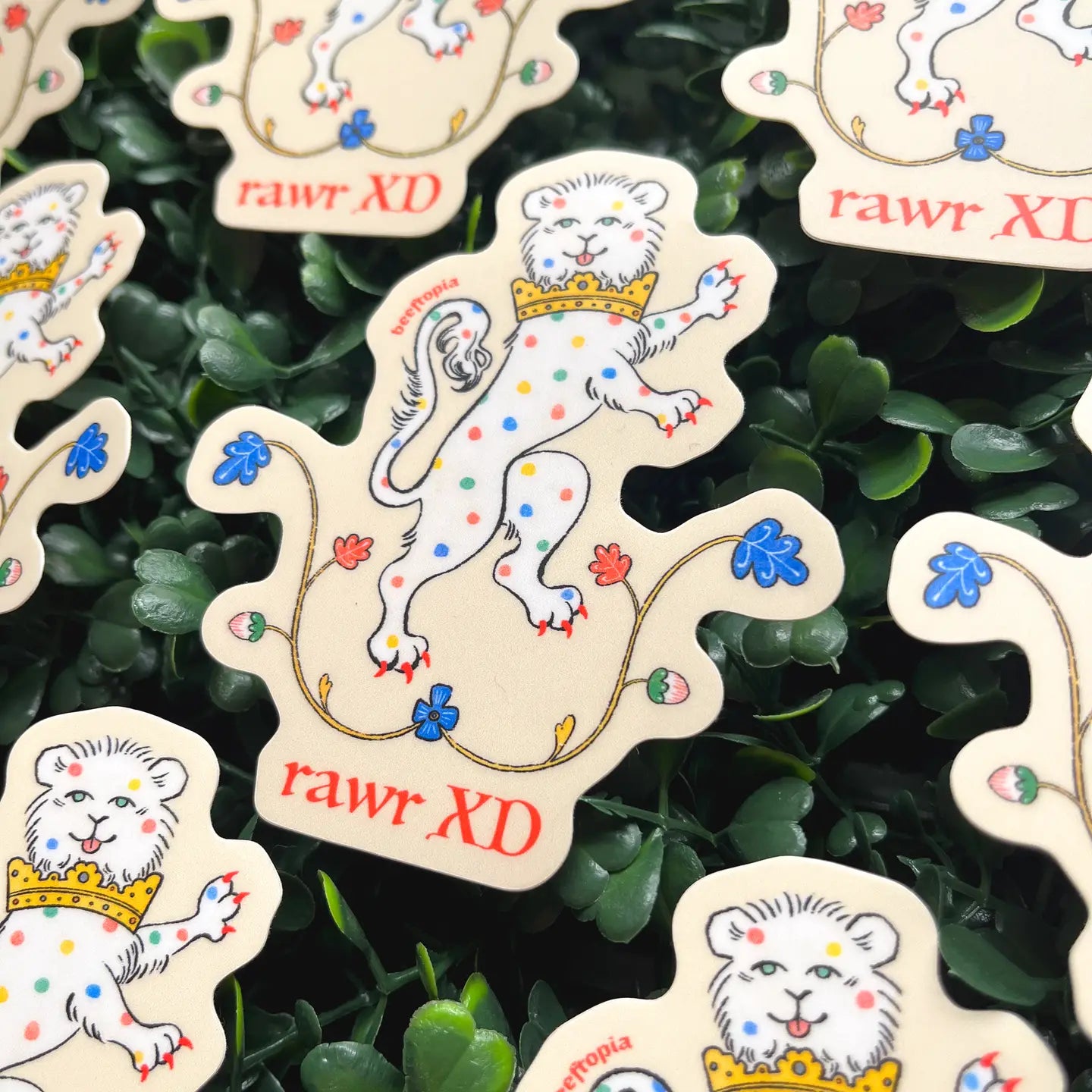 Beeftopia Medieval Lion Sticker—waterproof vinyl, crowned lion, colorful spots, green foliage, "rawr XD" text. Durable décor.