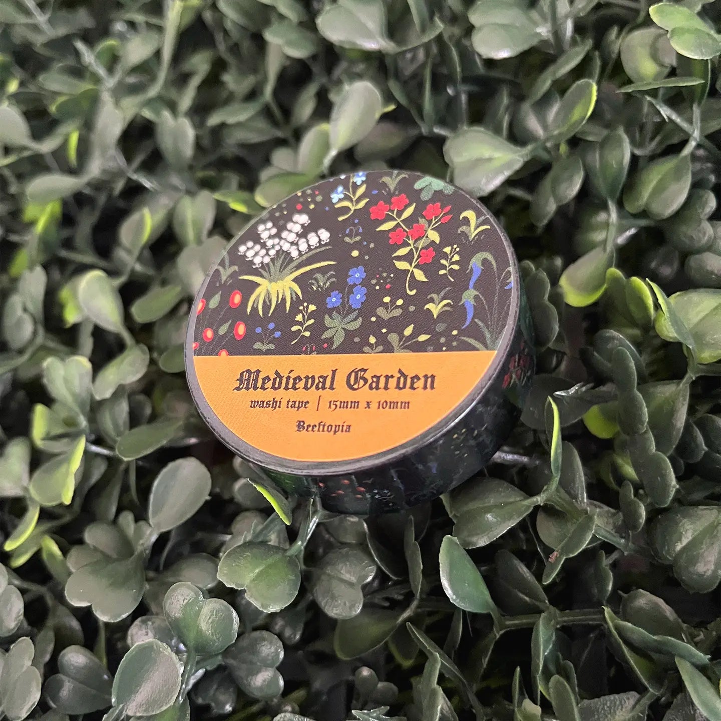 Beeftopia Medieval Unicorn Garden Washi Tape decorates a small round tin on vibrant green leaves—unique craft supplies container.