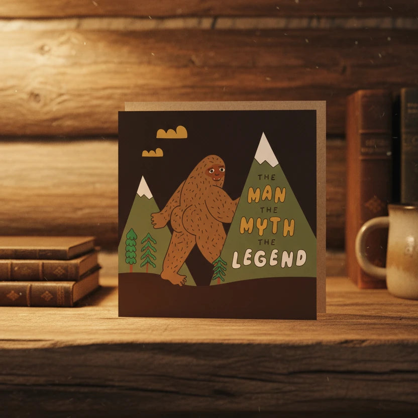 Funny Betiobca Bigfoot greeting card, "The Man, The Myth, The Legend," with cryptid humor on rustic wooden table.