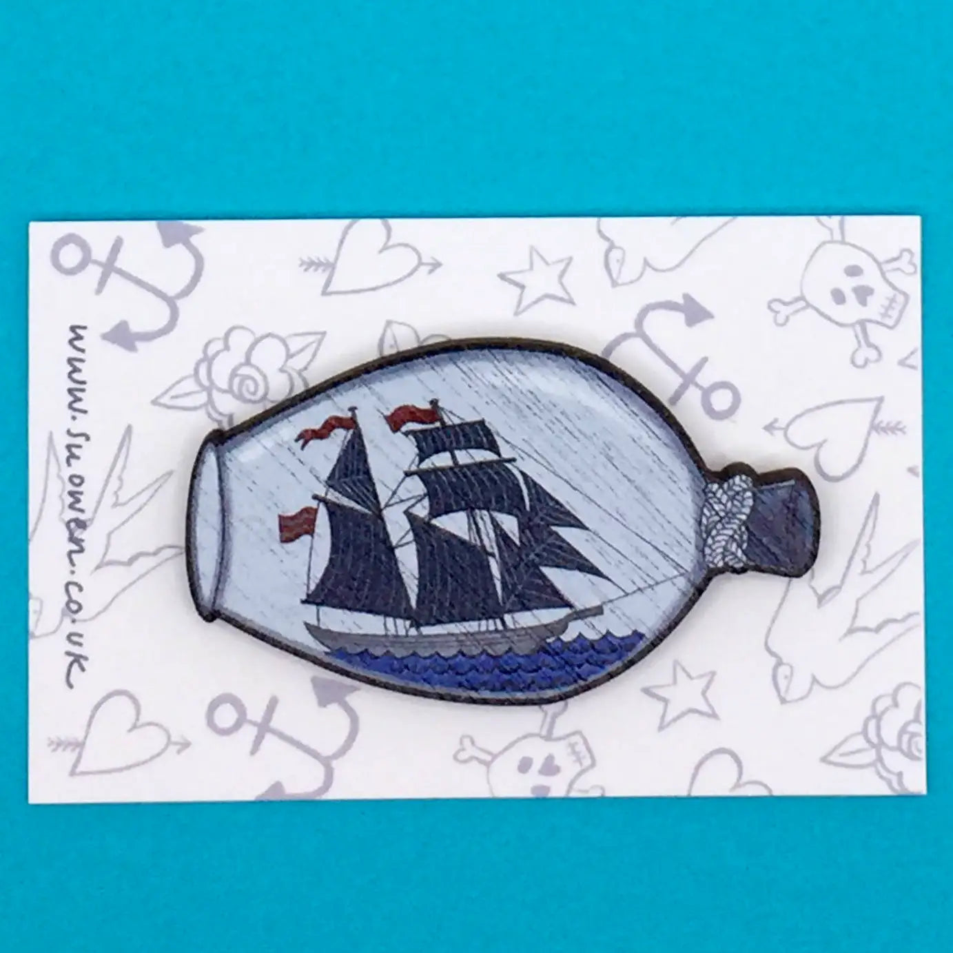 Original illustration by Su Owen of a ship with sails inside a bottle against a bright blue background, featured on the Su Owen Nautical Boat In Bottle Pin Brooch crafted from sustainable walnut.