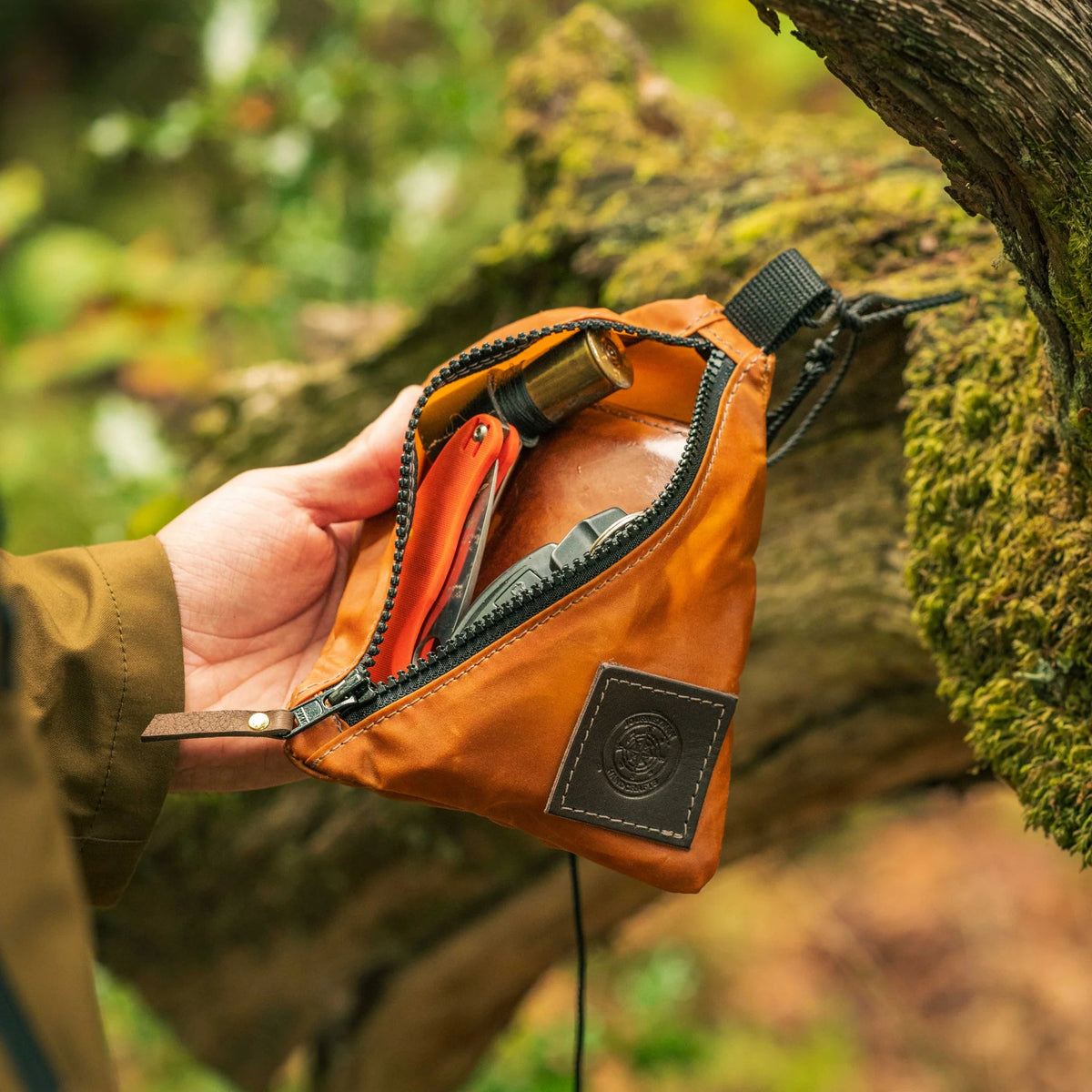 Forager Provisions LTD Journeyman Handcraft orange waxed canvas X-Pouch with diagonal zip held against a mossy log