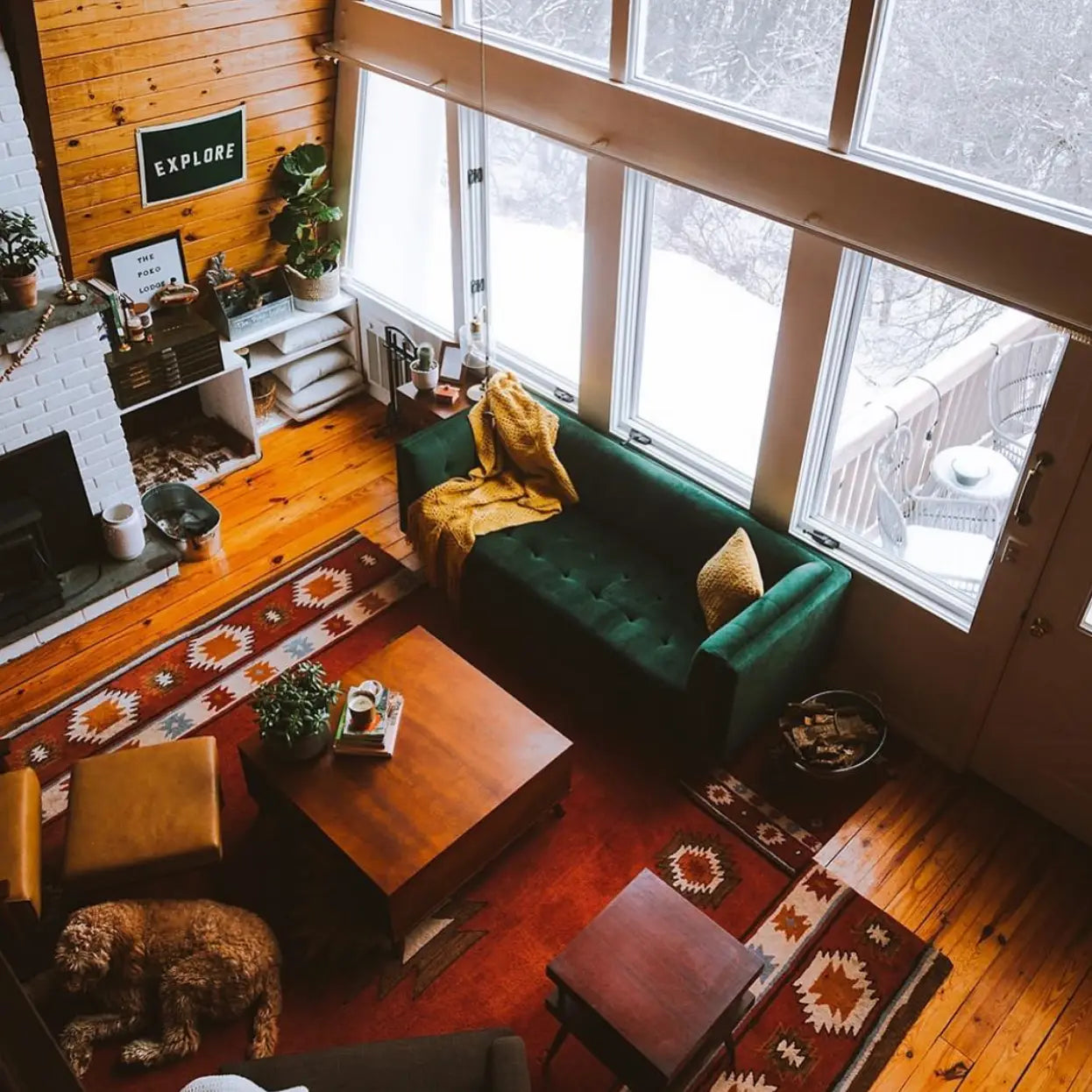 Cozy living room with green sofa, wooden furniture, colorful rug, and Oxford Pennant EXPLORE camp banner wall decor.