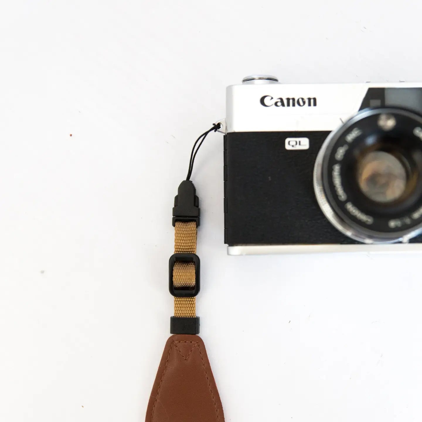 Canon film camera with brown Wildtree strap and adaptors on white background, vintage photography gear, classic 35mm accessory.