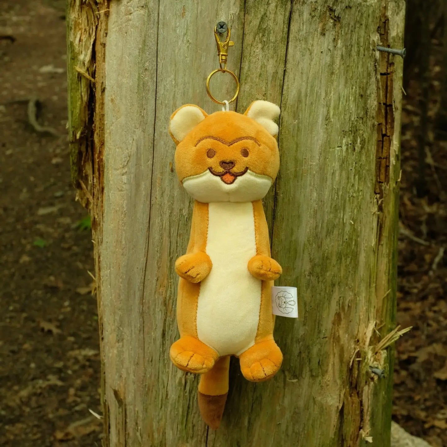Plush keychain shaped like a cartoon stout hanging on a wooden post.