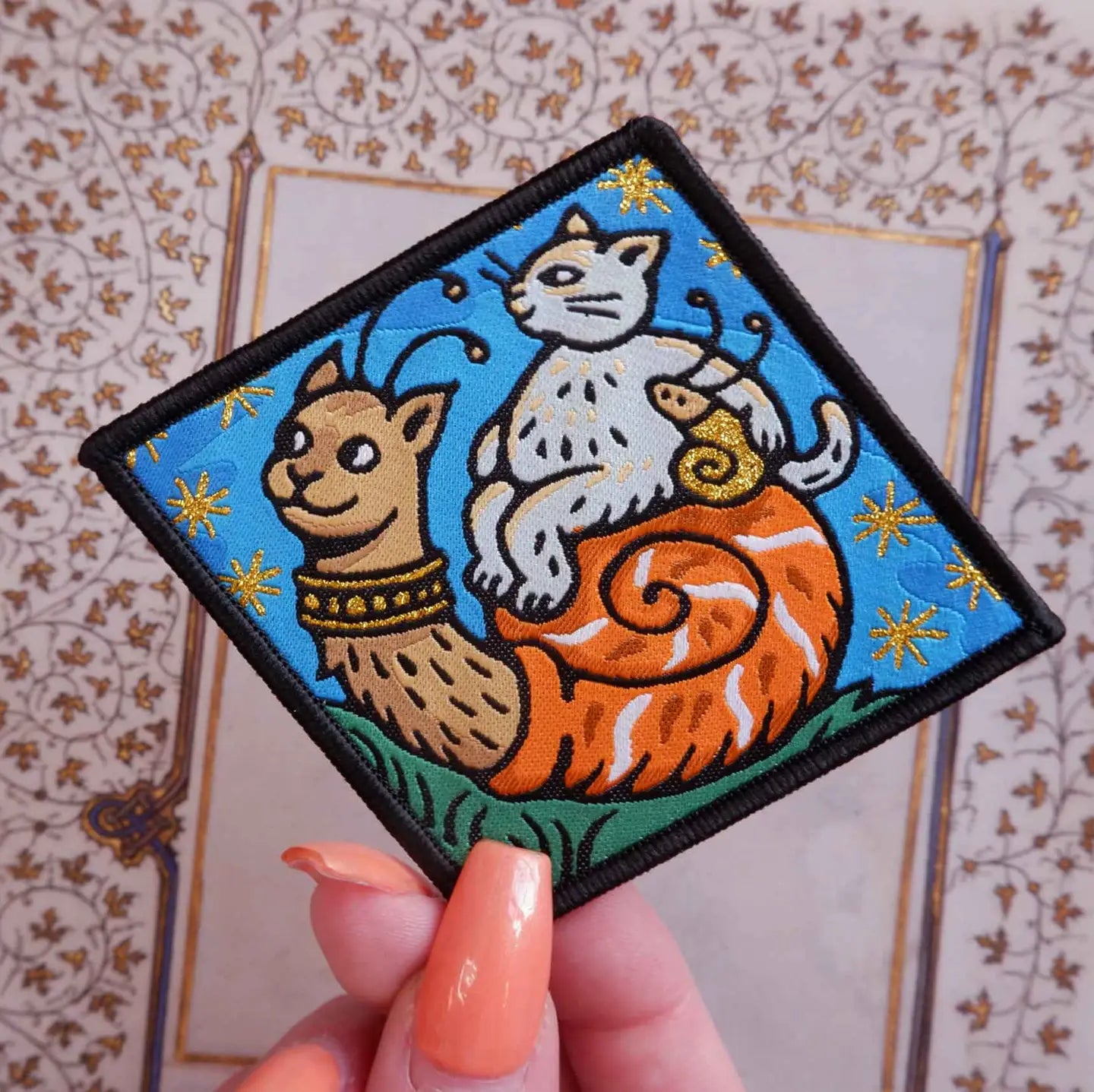 Hand displays Cat Coven Chosen Family woven patch—cat riding snail on blue and gold. Unique cat lover collectible accessory.