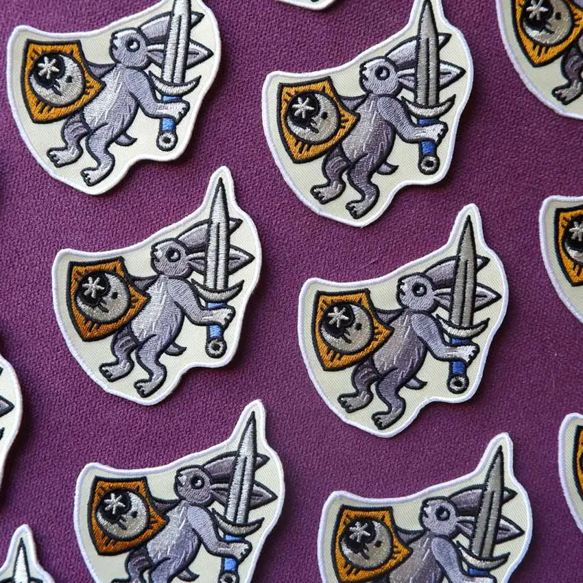 The Cat Coven Warrior Rabbit Patch by Forager Provisions LTD shows a gray rabbit with sword, shield on purple background.