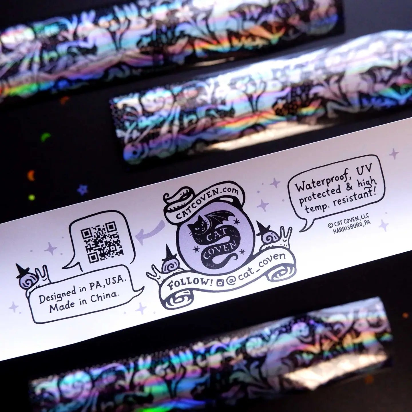 Cat Coven label with QR code and details beside a Cat Coven Rabbits vs Skeletons holographic sticker. Unique gothic merch.