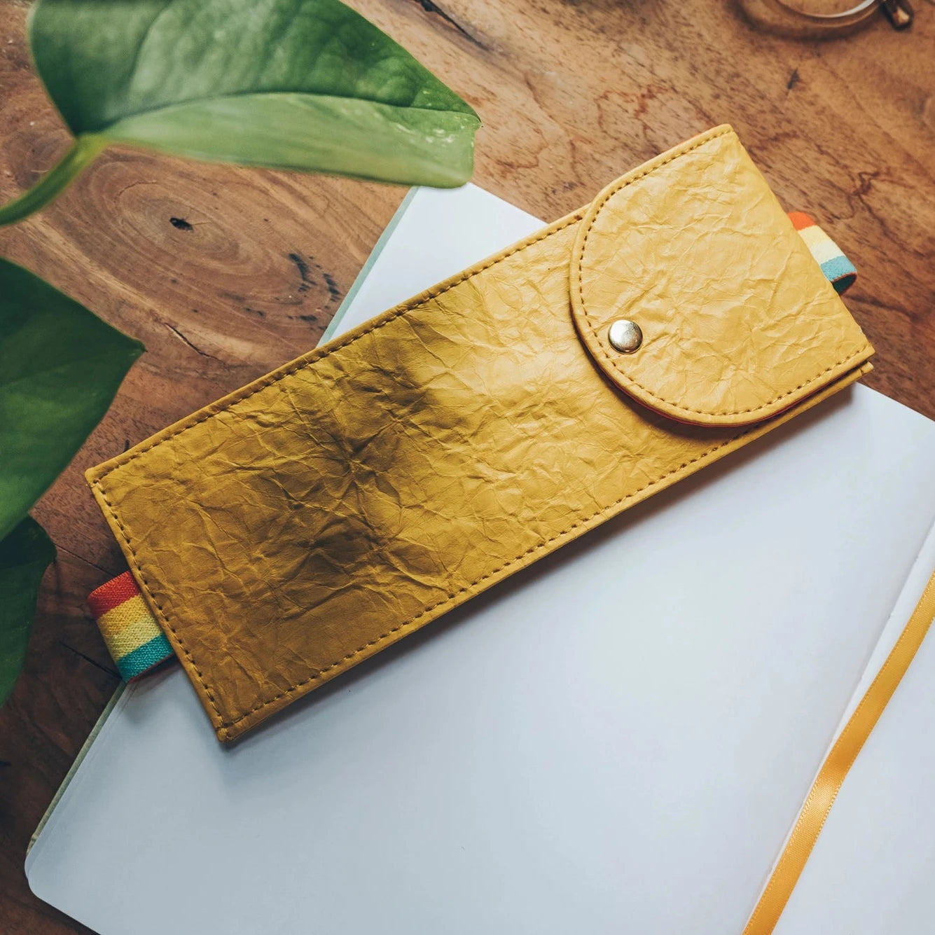 Denik Yellow Crinkle Notebook and Vegan Leather Pouch on desk near green plant—chic eco office supplies for stylish workspace.