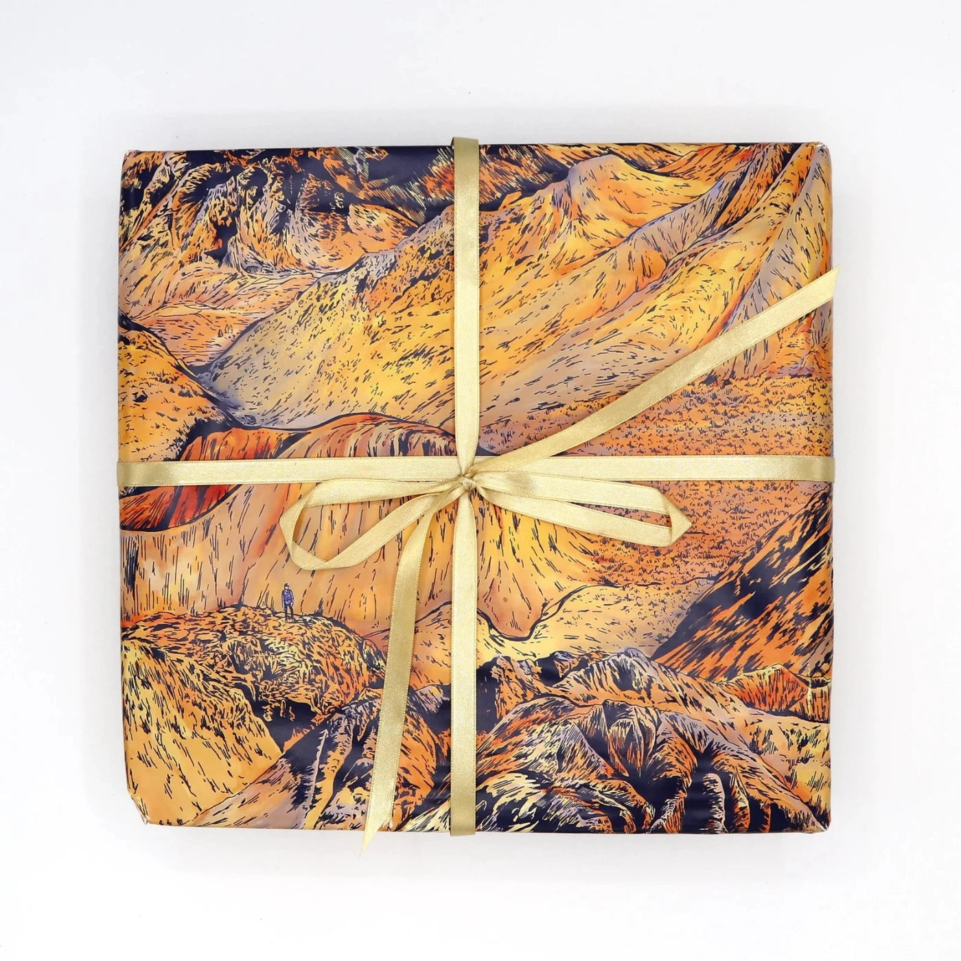 A wrapped present in orange and navy wrapping paper with an all over print of mountains finished off with a yellow ribbon bow