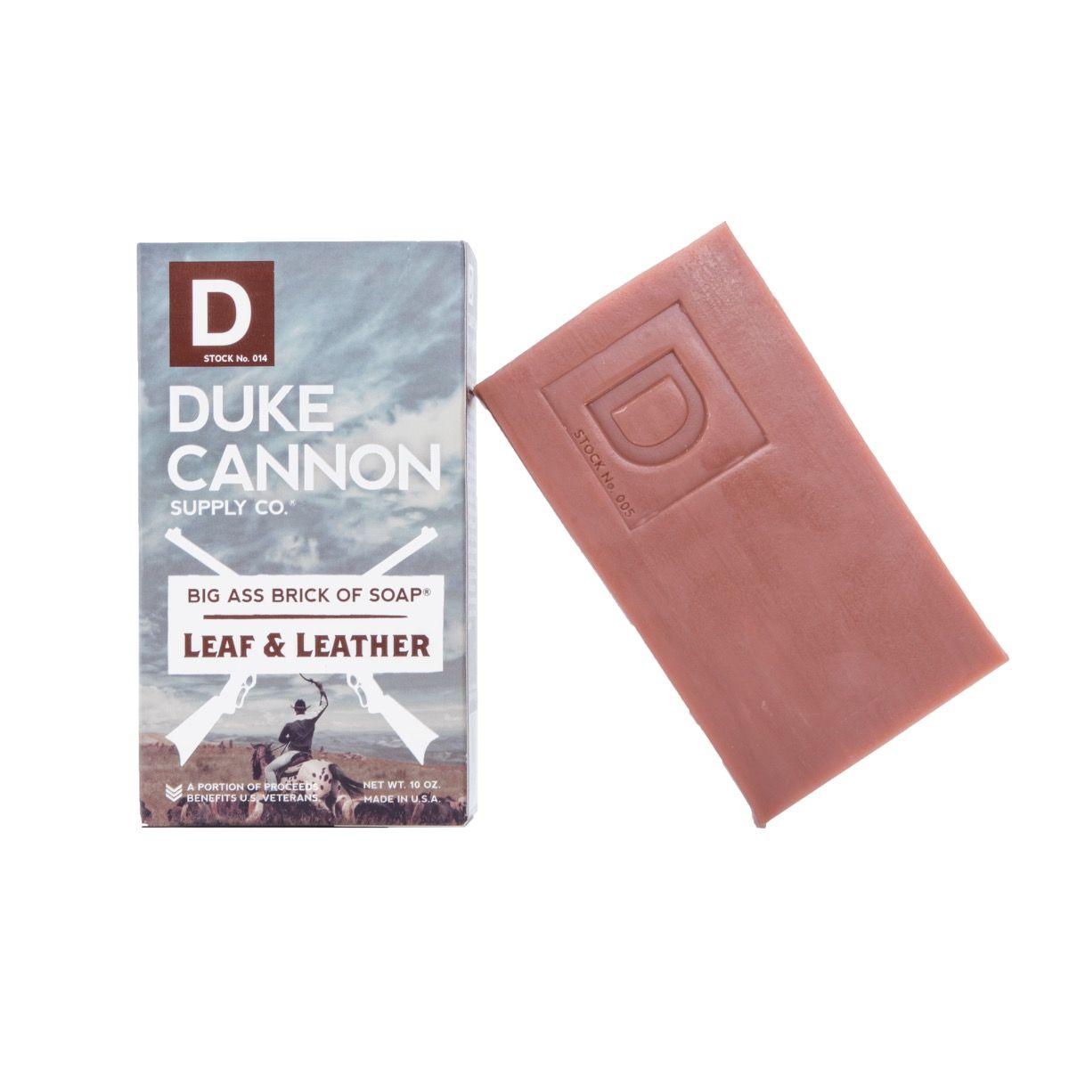 The packaging of Duke Cannon Big Ass Brick Of Soap Leaf & Leather features a rugged outdoor background that underscores its masculine scent and substantial size while also emphasizing its American-made quality and benefits for veterans.
