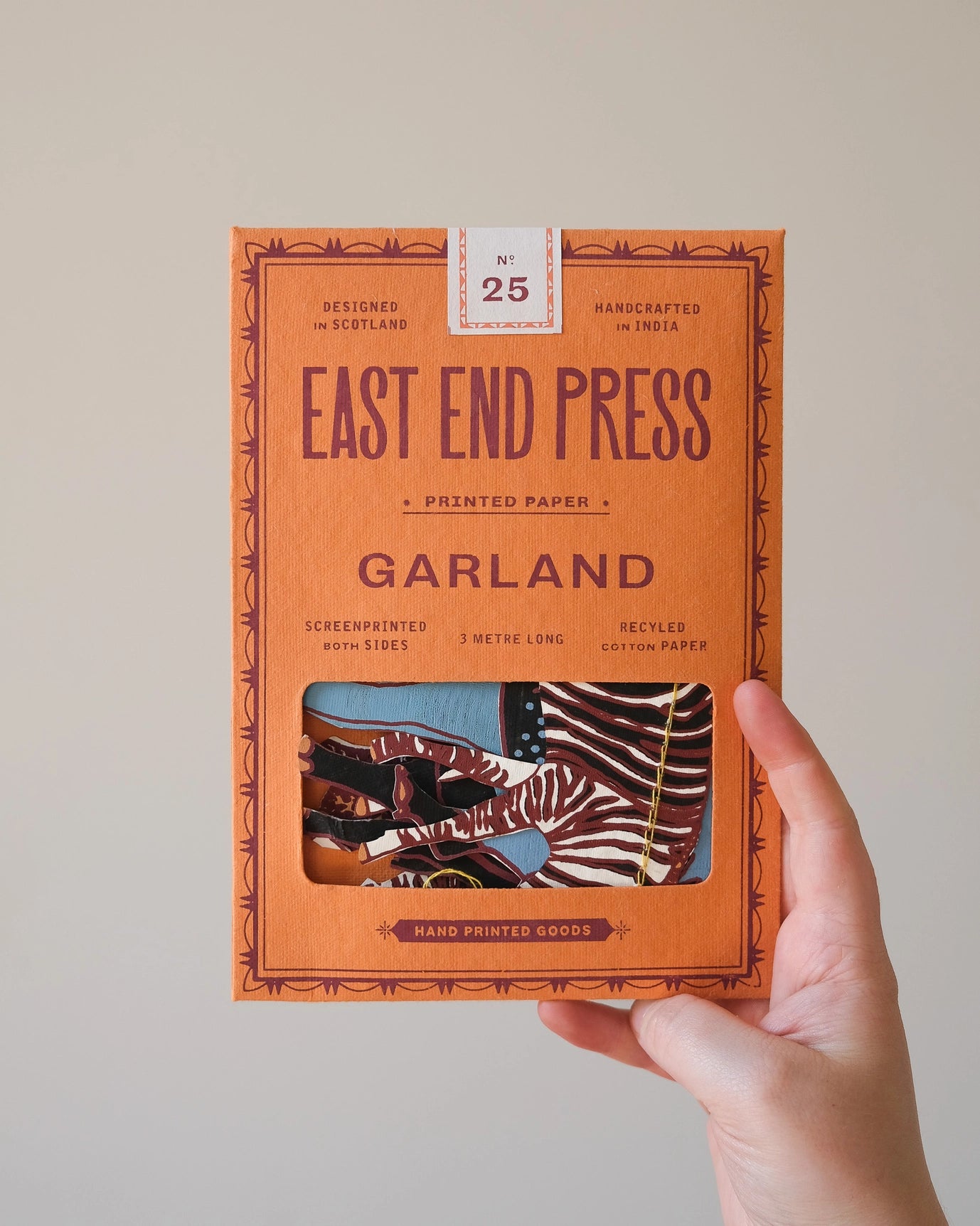 Hand holds East End Press Safari Animals Garland box with handcrafted zebra decorations; eco-friendly party décor.