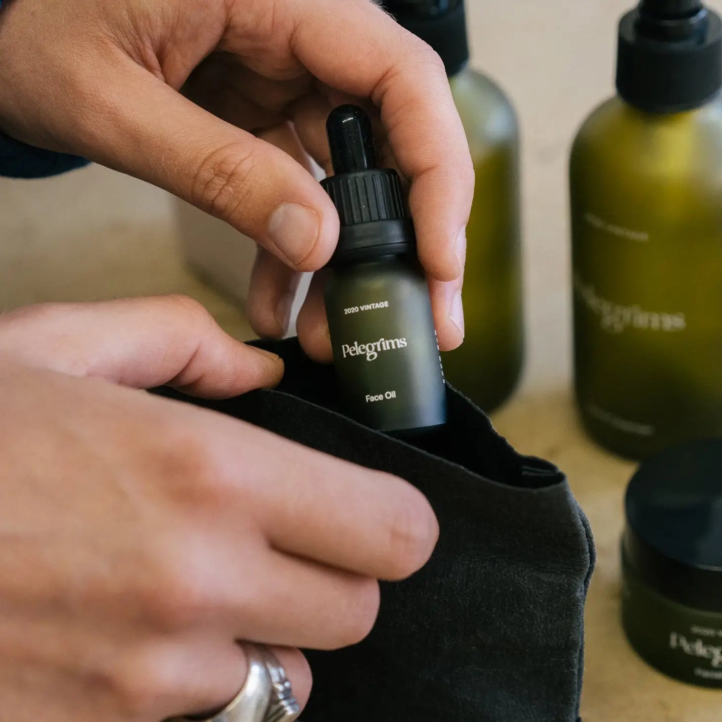A black toiletry bag featuring Pelegrims branding, containing travel sizes of facial balm and hand pomade, along with a dropper bottle of facial oil infused with Pinot Noir Grape Extract, known as the Pelegrims Exploration Set.