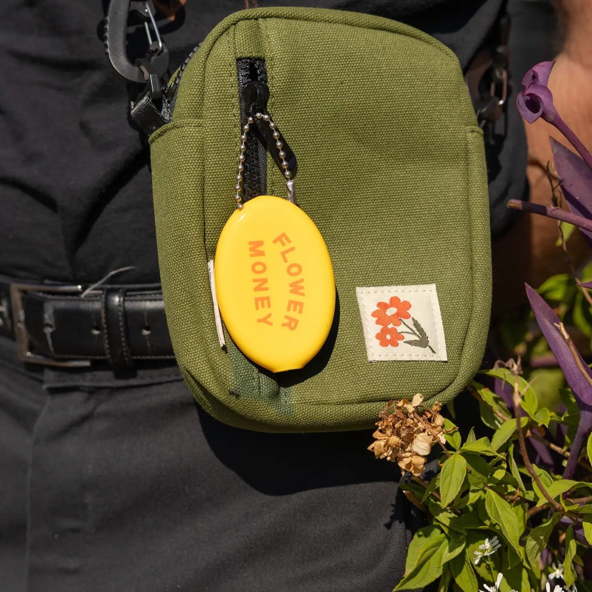 The Three Potato Four Flower Money Coin Pouch and yellow keychain next to lush green plants; unique floral accessory set.