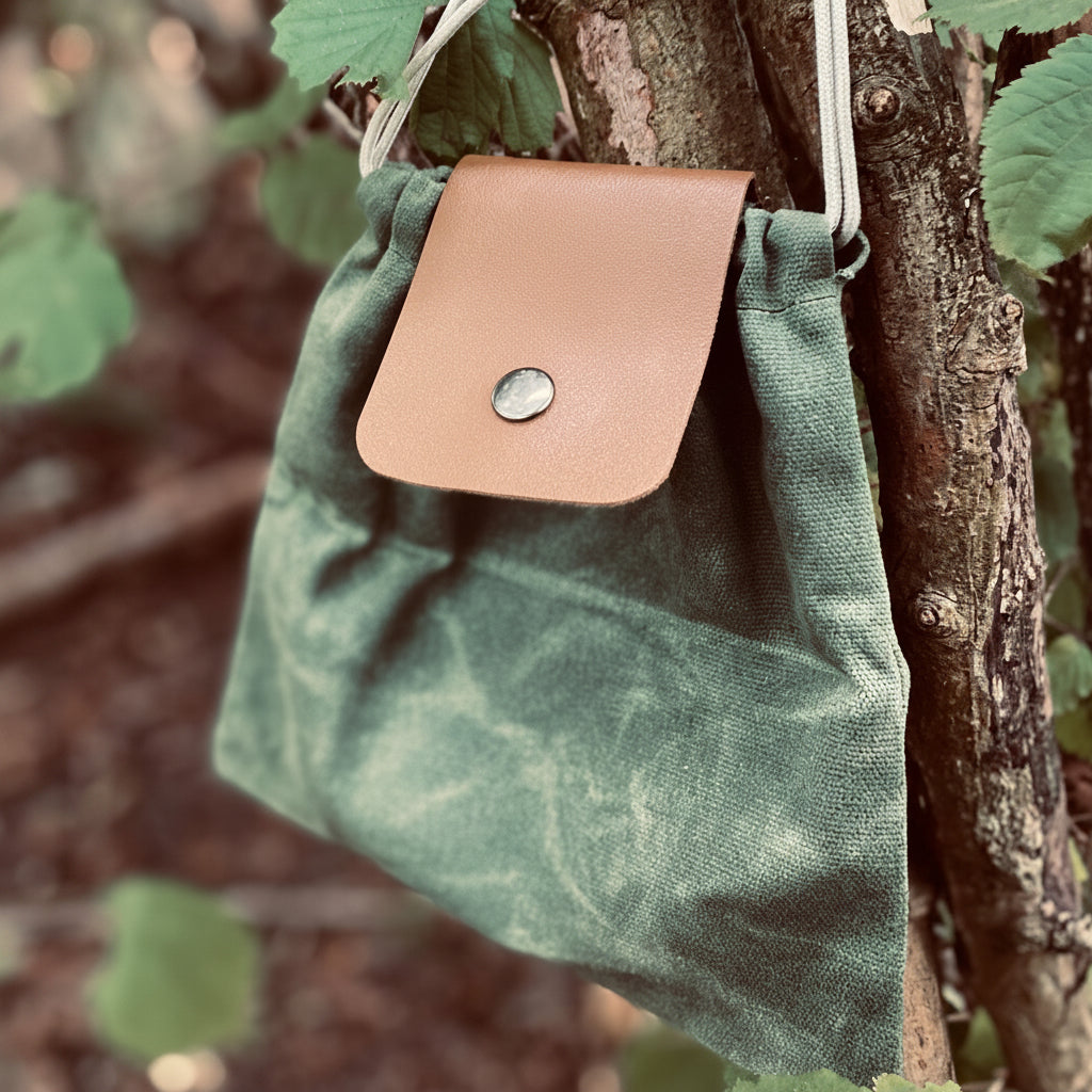 Forager Provisions LTD green up-cycled cotton canvas pouch with a vegan faux leather flap hanging on a tree branch.