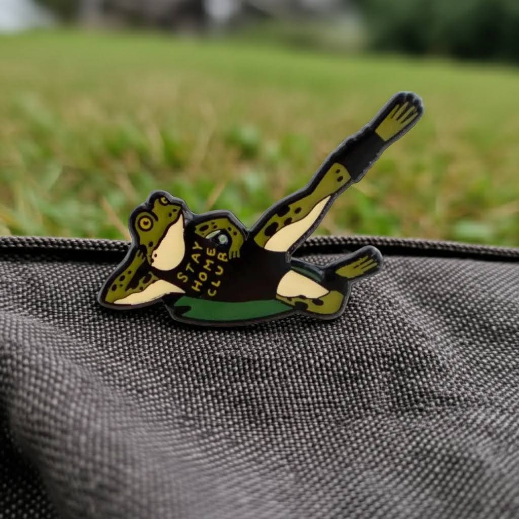 Forager Provisions LTD Stay Home Club enamel pin featuring a green frog doing a leg lift exercise on a grey bag