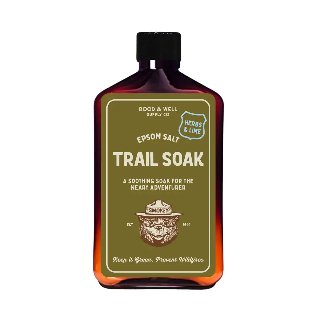 Brown bottle of Good & Well Supply Co Smokey Bear Trail Soak bath salts, labeled Herbs & Lime, for relaxing herbal bath.