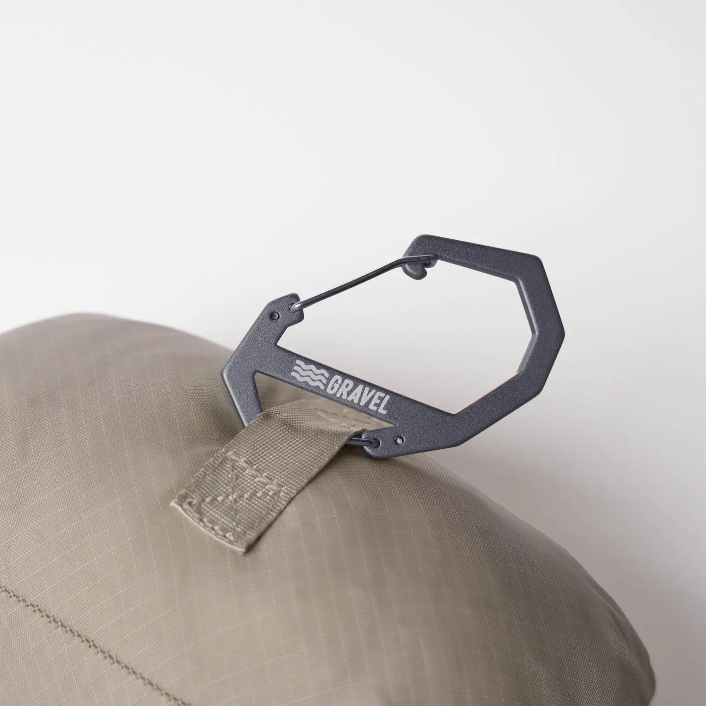 Black carabiner attached to a beige cap with 'Bravel' branding on a light gray background