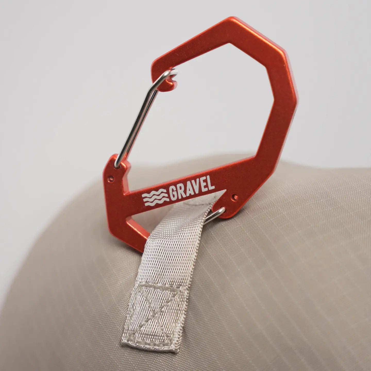Orange carabiner with a strap attached, featuring the brand 'Gravel', on a beige surface