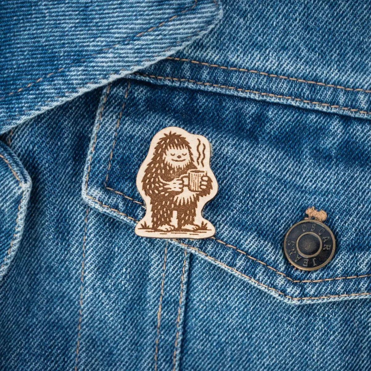 Forager Provisions LTD Hey Bear Outdoors wooden Bigfoot pin badge attached to a blue denim jacket pocket.