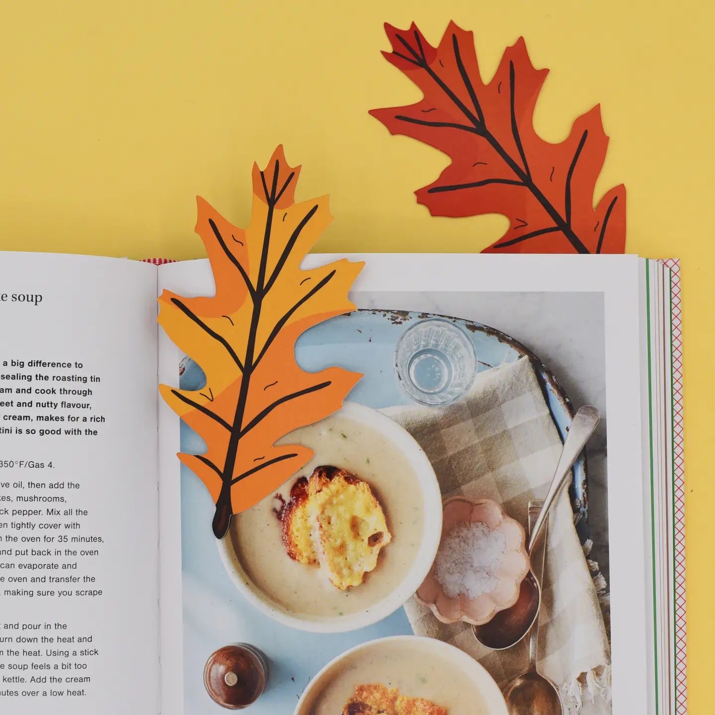 Open cookbook with two autumn leaf bookmarks on yellow background – perfect for cozy fall recipes, reading, book lover gifts.