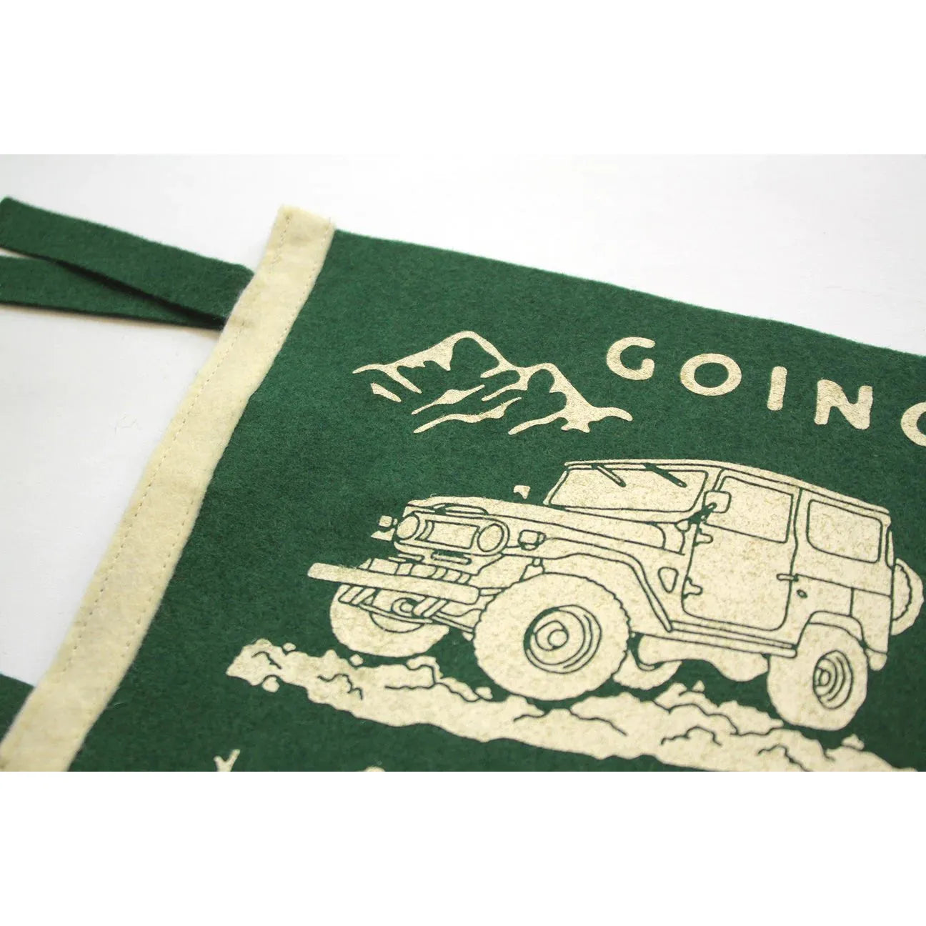 A green fabric with a beige border, printed with an image of an off-road vehicle and mountains, partially displaying the words "Going to the Mountains," inspired by a John Muir quote, from the Oxford Pennant Going To The Mountains collection.