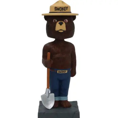 Smokey Bear bobblehead with ranger hat, jeans, and shovel on gray baseācollectible fire safety mascot figurine for fans.