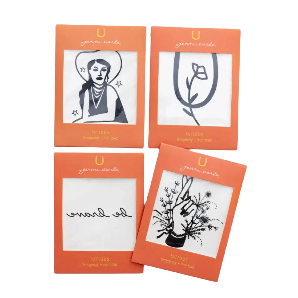 Four non-toxic temporary tattoos packaged in an orange envelope include designs of a woman with a hat, a rose, the words "go brave", and an intricate floral hand with leaves. Perfect for adding western vibes to any look, these Jenni Earle Cowgirl Dreamin' Temporary Tattoos bring a touch of adventure wherever you go.