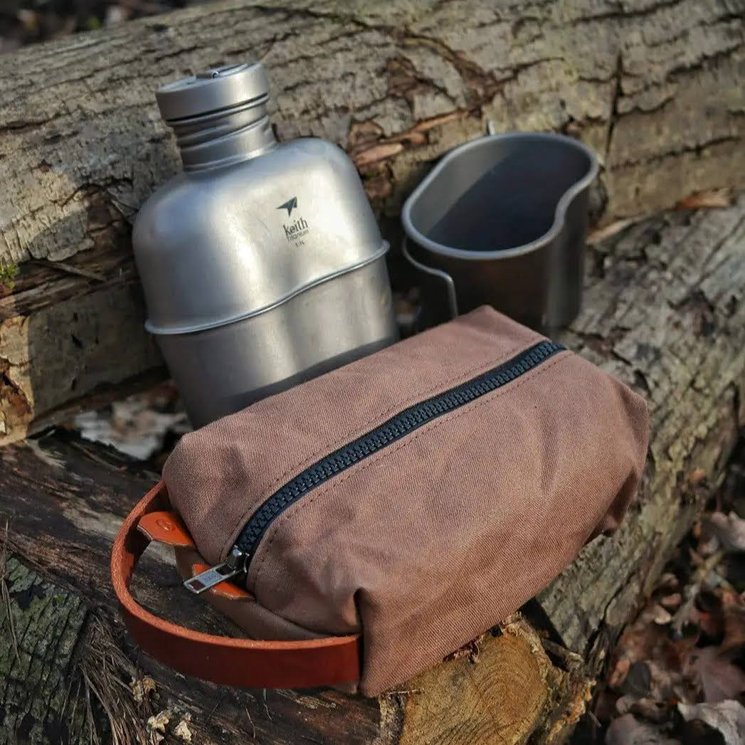 Forager Provisions LTD Journeyman Handcraft brown canvas toiletry bag with YKK zipper and grab loop on a wooden log.