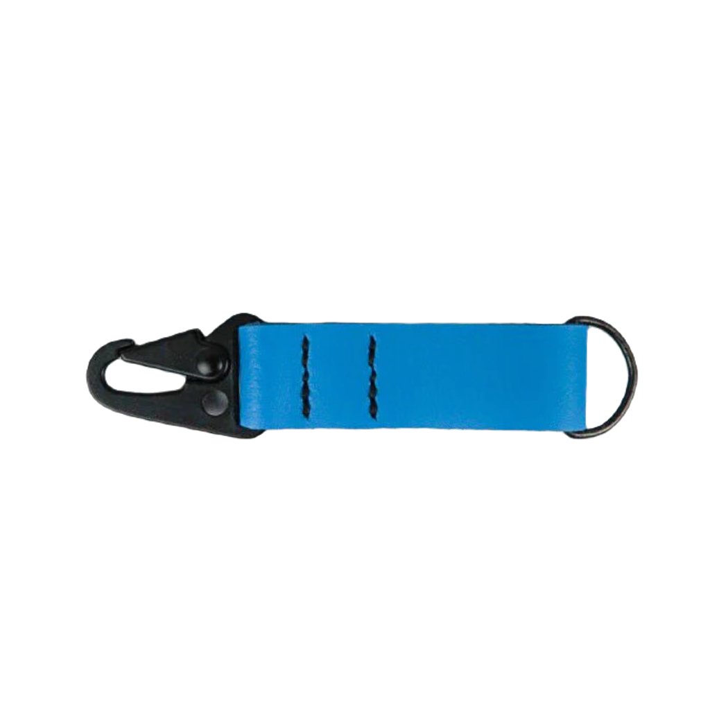 A blue Kjøtt Supply Co Key Fob, featuring a black metal hook, a black button, and the label "KOTT SUPPLY CO." against a white background, crafted from premium leather and backed by a lifetime warranty.
