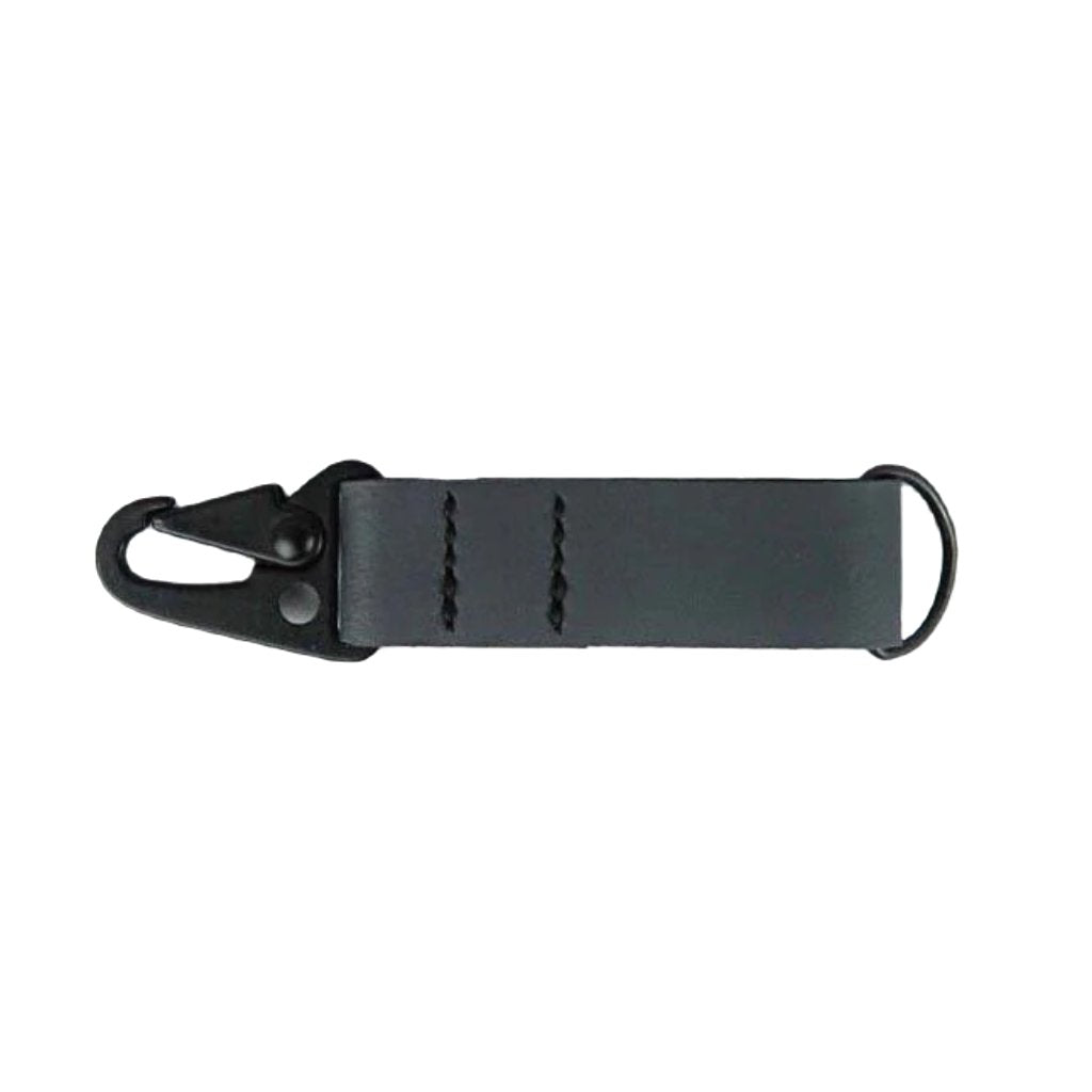 A blue Kjøtt Supply Co Key Fob, featuring a black metal hook, a black button, and the label "KOTT SUPPLY CO." against a white background, crafted from premium leather and backed by a lifetime warranty.