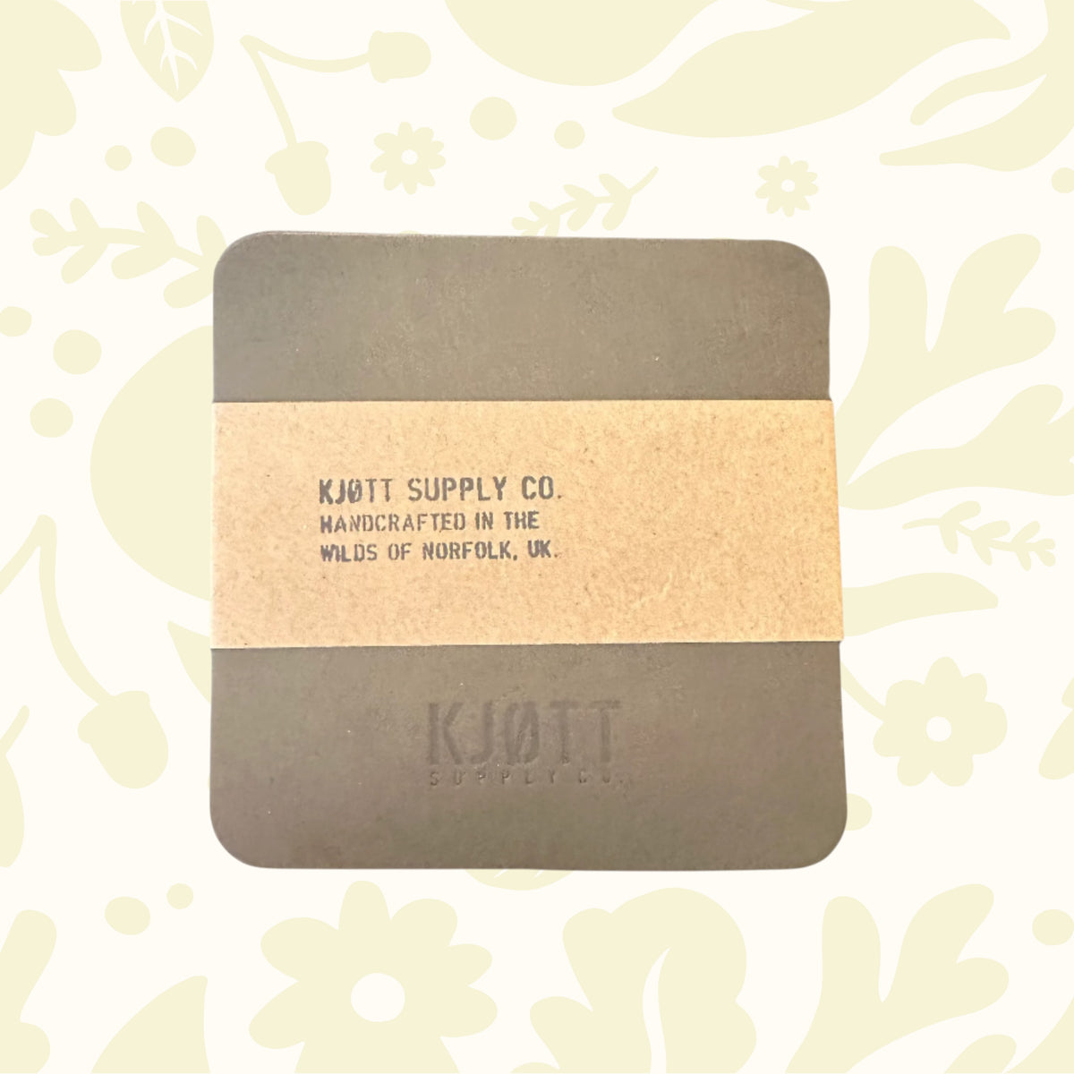Khaki green leather coaster by Kjøtt Supply Co., square with branded details and tan band, luxury drink accessory.