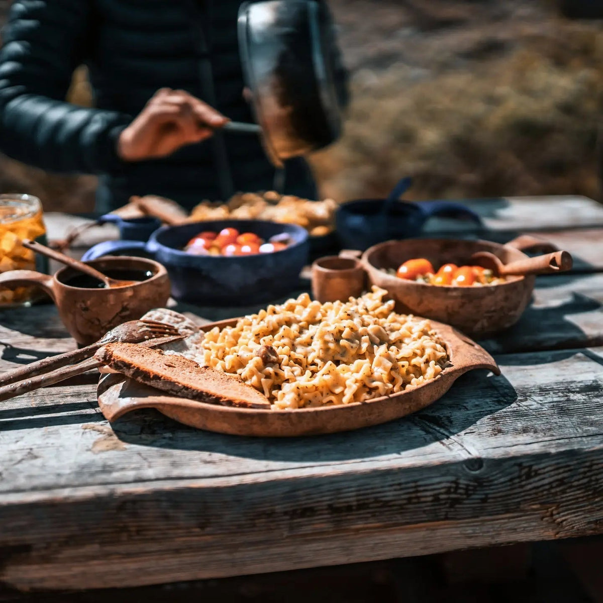Outdoor dining with pasta on a Kupilka 44 Large Plate, surrounded by other dishes and a person enjoying an al fresco meal.