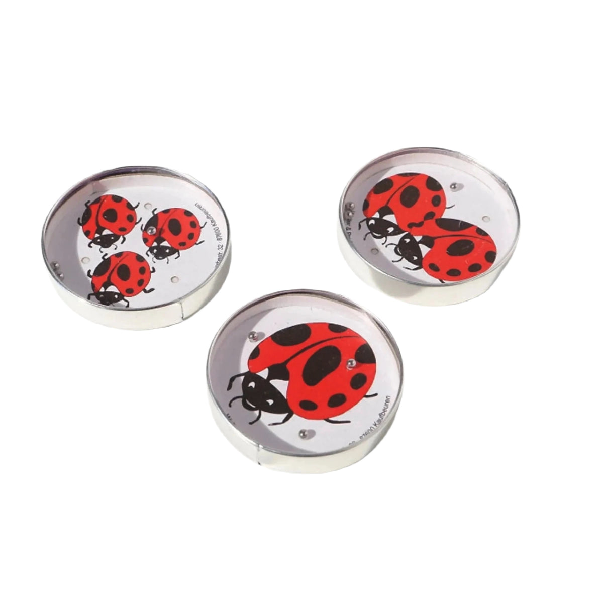 Three small circular containers with red ladybug illustrations on white backgrounds, placed on a white surface, call out to puzzle enthusiasts. One of them cleverly holds a hidden Die Blechfabrik e.K Ladybird Puzzle Ball Maze (Random) game inside.