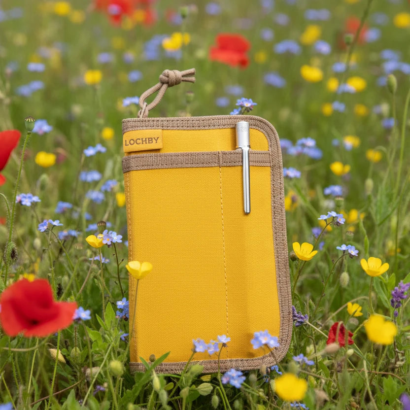 Forager Provisions LTD Lochby mustard pocket journal with a silver pen in a vibrant wildflower meadow.