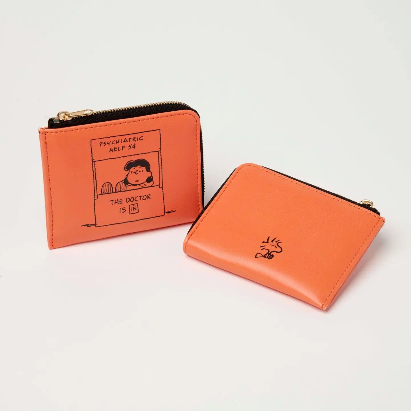 Two orange vegan wallets by Magpie: Peanuts Self-Care Money wallet and orange wallet with cloud design on clean background.