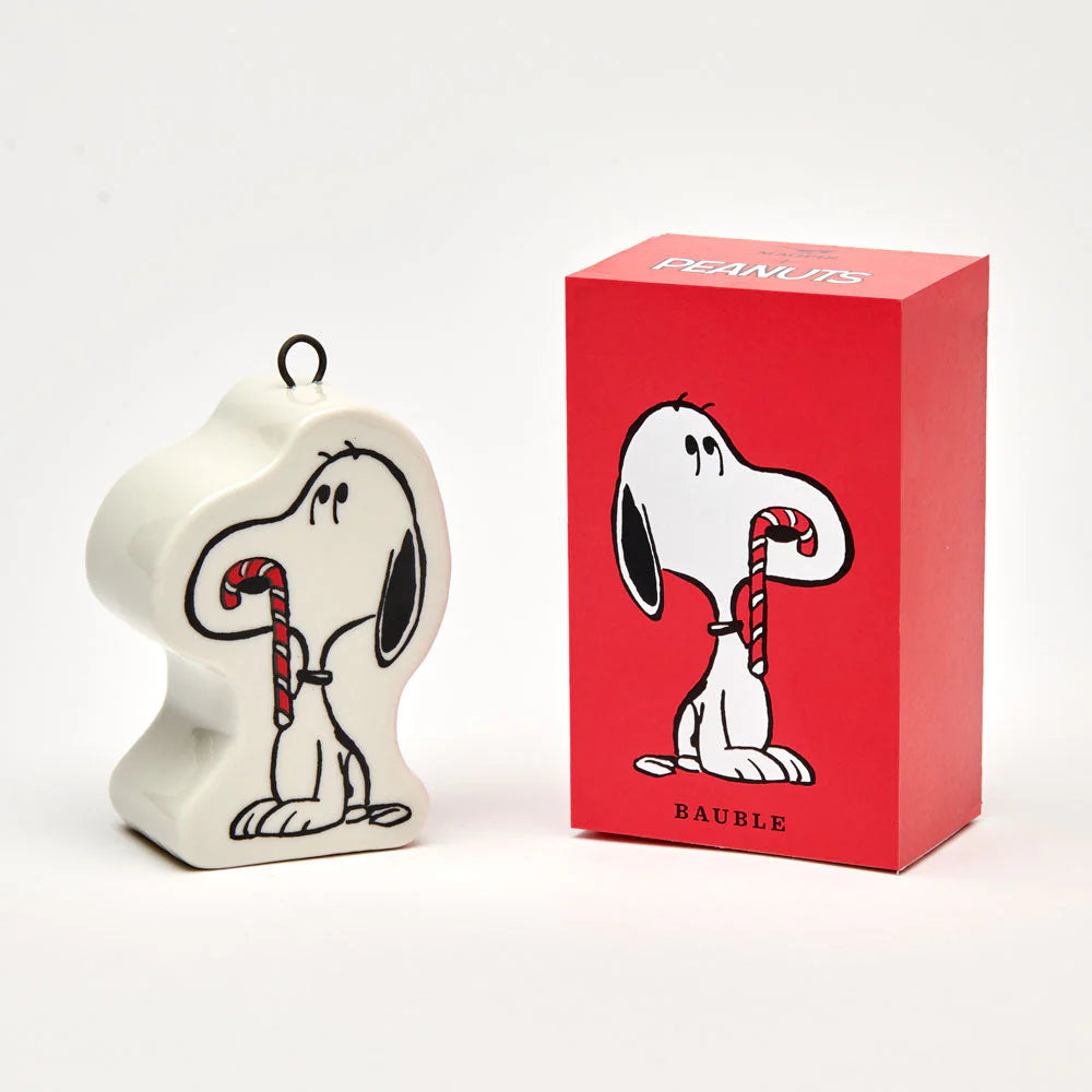 A ceramic shaped decoration with a metal hook for hanging. Image is an illustrative black and white snoopy with a red and white candy cane hanging from his nose. Comes in a red box with the words bauble.