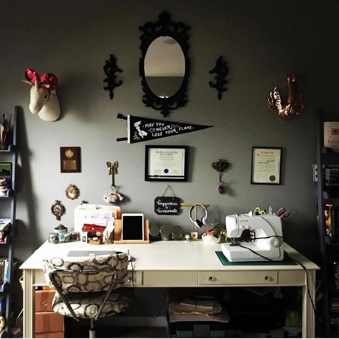 Vintage sewing desk with Oxford Pennant May You Never Lose Your Flame, sewing machine, and wall art for creative workspace charm.