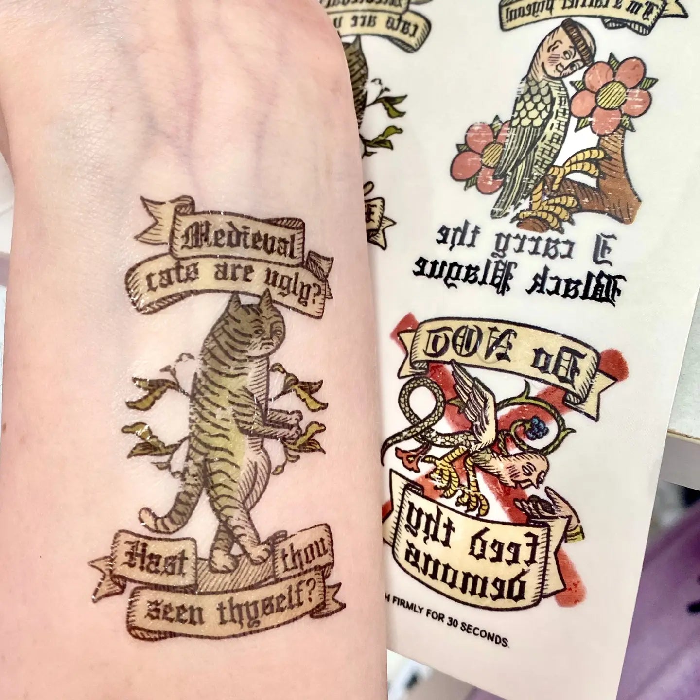Forager Provisions LTD Clarice Tudor medieval cat temporary tattoo applied on a wrist with sticker sheet visible.