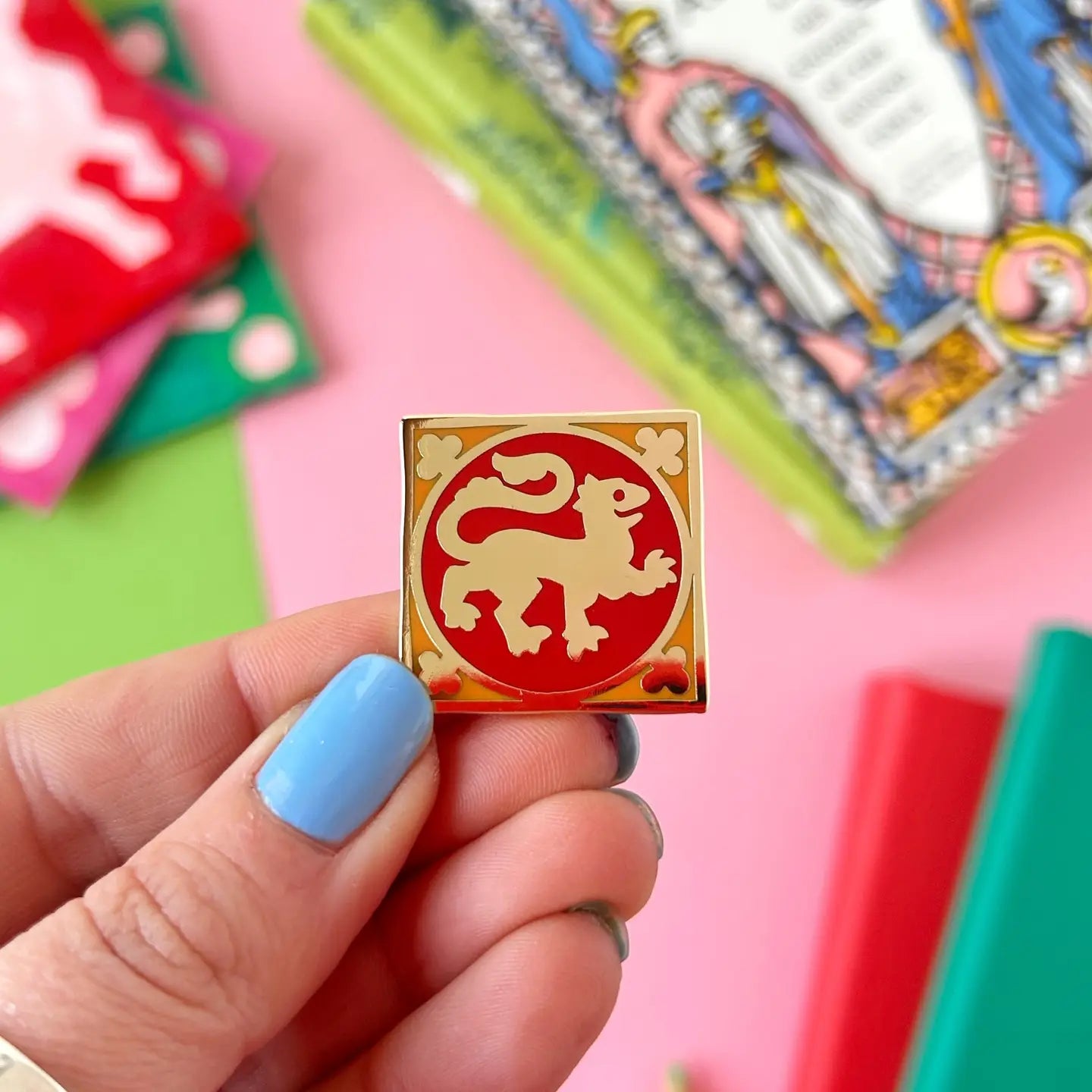 Hand with blue nails holds Stacey McEvoy Caunt Lion Medieval Tile Pin, a unique medieval art-inspired enamel accessory.