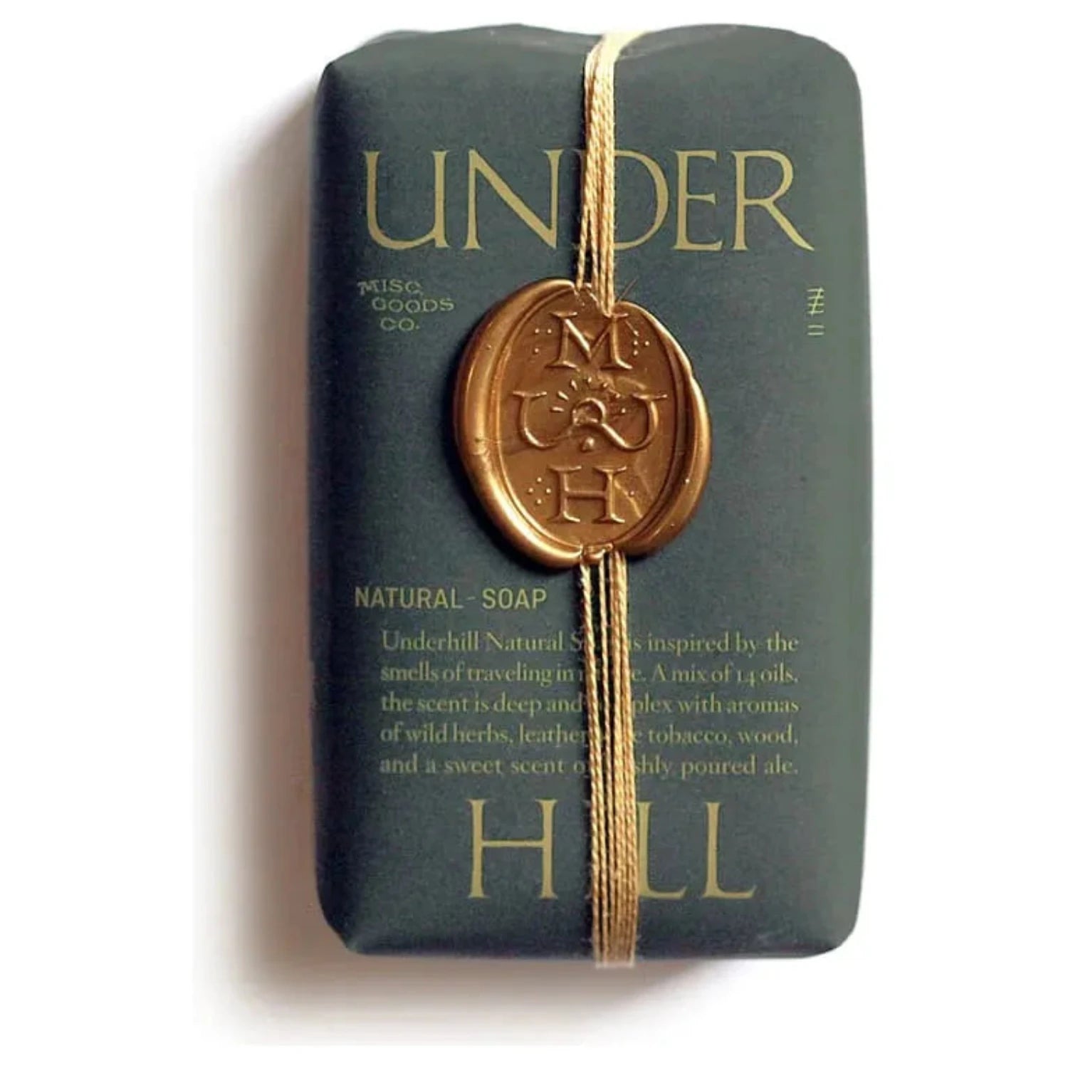 A bar of Misc Goods Co Underhill Soap, handcrafted in the USA and vegan-friendly, elegantly wrapped in dark paper with gold string and sealed with a gold wax stamp marked "M G & H.