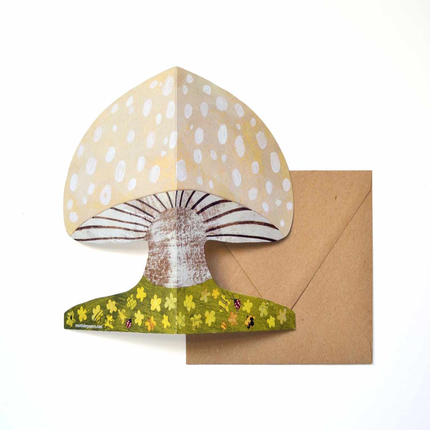 A image of a illustrated mushroom in light beige and white spots in a flower bed with ladybugs placed on a brown envelope.